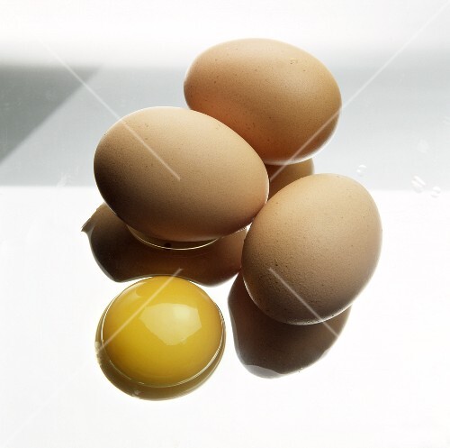 Three brown eggs and one egg yolk on a sheet of glass