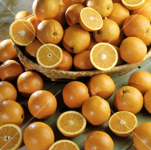 Many whole & halved oranges in and in front of a basket