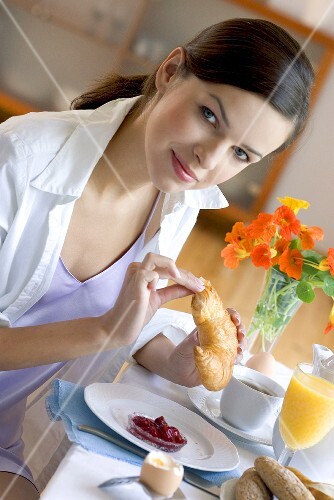 Young woman at breakfast table eating croissant