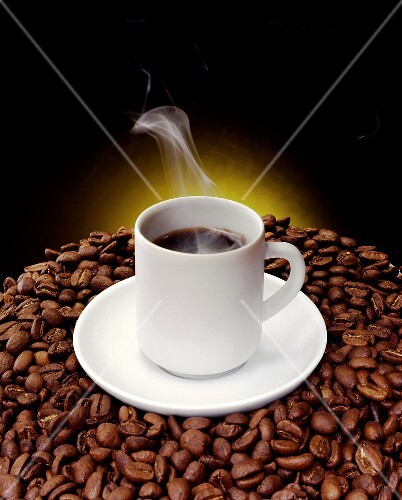 Cup of steaming coffee on coffee beans