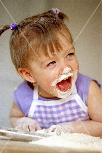 Small laughing girl baking with flour on her face (2)