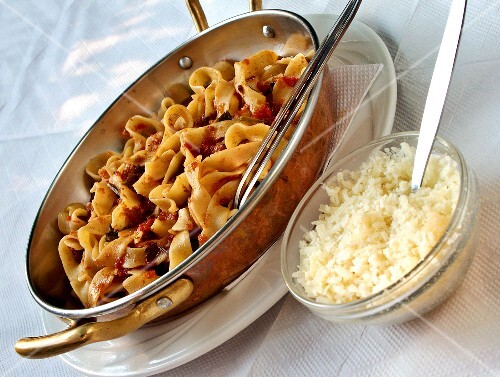 Ribbon pasta with tomato sauce, grated hard cheese beside it
