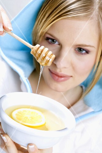 Young woman letting honey run into lemon tea