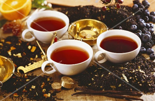 Three fruit teas in cups with tea leaves and berries