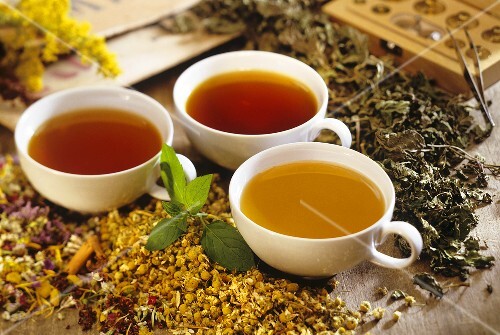 Three medicinal teas in cups with dried medicinal herbs