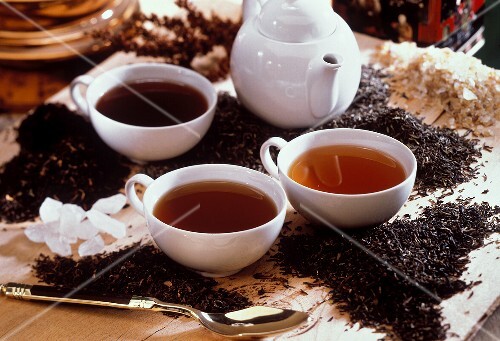 Three black teas in cups between tea leaves and crystal sugar