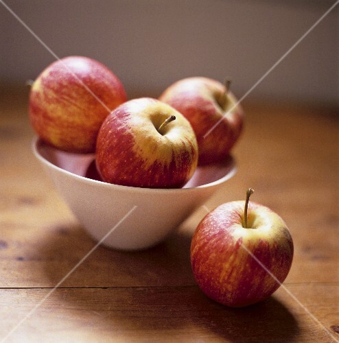 Red apples in a bowl and one beside it on a wooden table