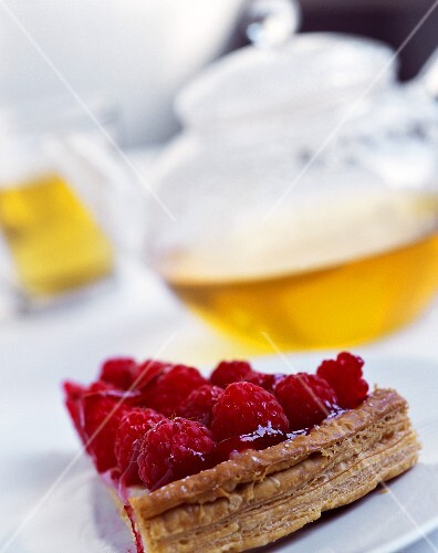 Piece of raspberry flan in front of teapot