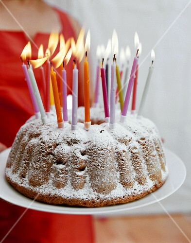 Woman serving birthday gugelhupf with burning candles