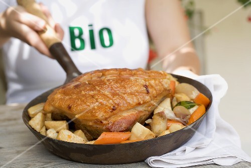 Woman holding pan of organic roast pork & root vegetables