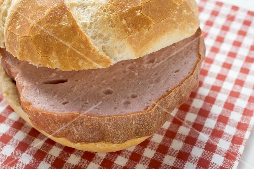 Slice of Leberkäse (type of meatloaf) in roll on paper napkin