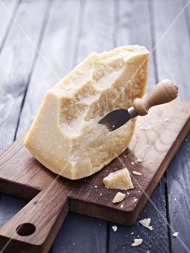 Piece of Parmesan cheese with cheese knife on chopping board