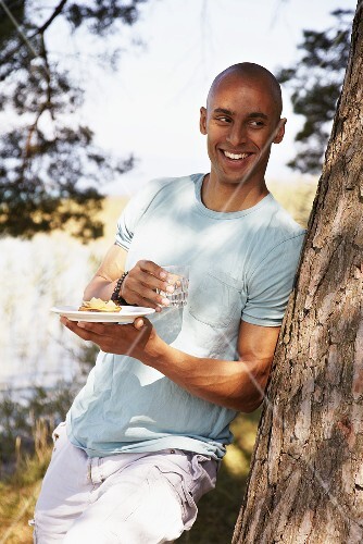 Young man standing by tree with crostini and glass of water