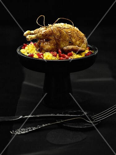 Quail with gold leaf on couscous with pomegranate seeds
