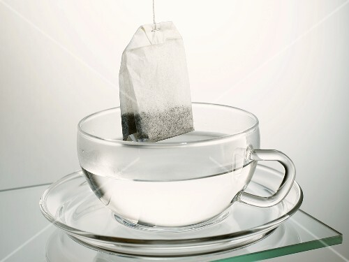 Tea bag hanging over a glass cup of hot water
