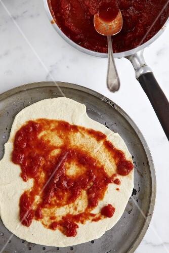 Pizza base with tomato sauce on baking tray (overhead view)