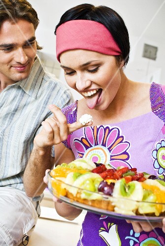 Woman with fruit tart licking cream from a man's finger