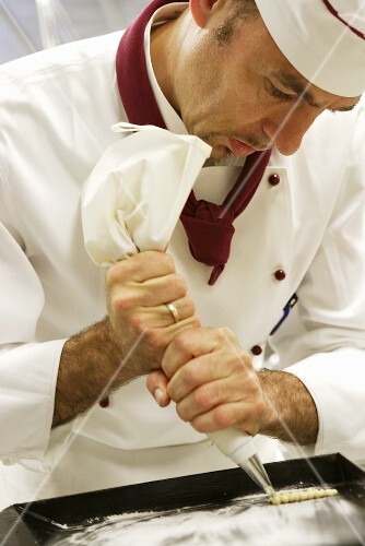 Chef piping pastry dough onto a baking tray
