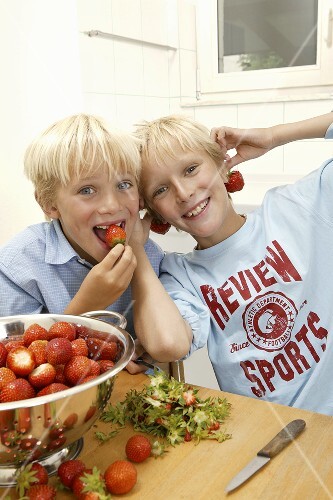 Two blond boys hulling strawberries