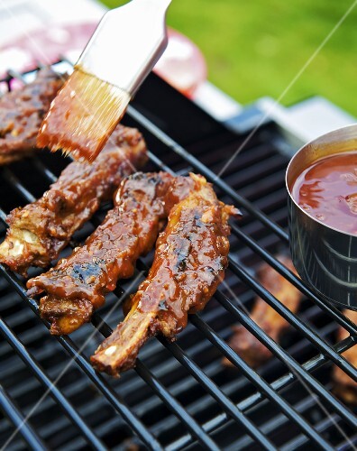 Brushing spare ribs on a grill with barbecue sauce
