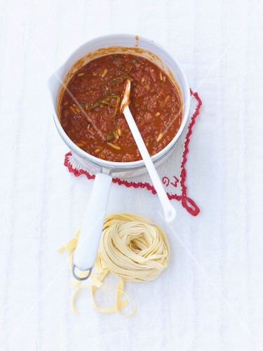Tomato sugo in a small pan and uncooked tagliatelle