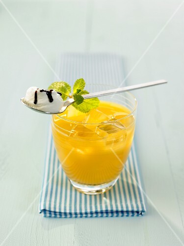 A glass of pineapple cocktail with whipped cream on a spoon