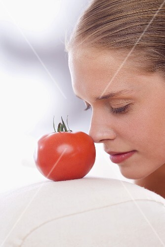 Young woman with the tip of her nose against a tomato