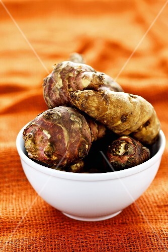 Jerusalem artichokes in bowl on orange background