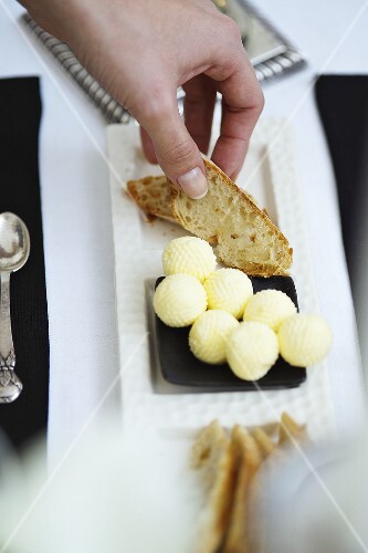 Hand greift nach Brotscheibe und Butter