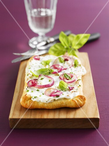 Pizza topped with soft cheese, onion rings and basil