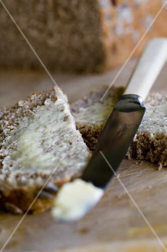 A halved slice of bread and butter with knife
