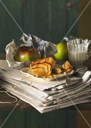 A piece of apple tart on newspapers with a jug of cream