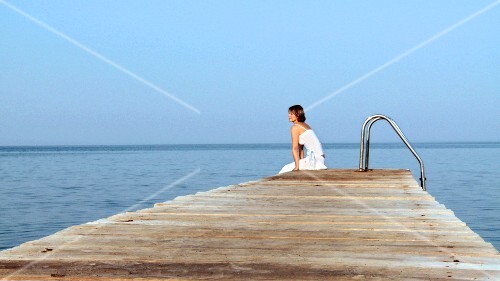 Young woman walking along landing stage and sitting down