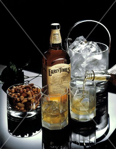 Whisky Being Poured into a Glass; Bottle of Whisky and Peanuts