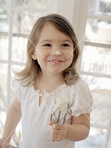 Small girl baking with blob of cream on her nose