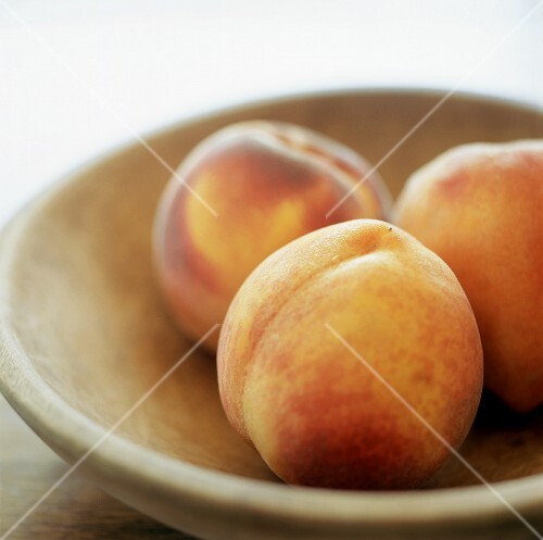 Three peaches in wooden bowl