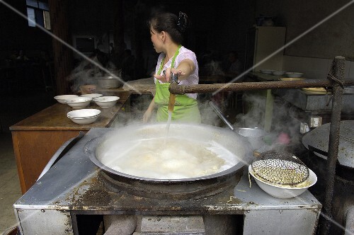 Asiatische Frau giesst Wasser in grossen Kessel