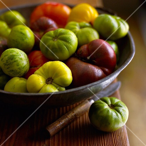 Bowl Full of Multi-Colored Heirloom Tomatoes on a Table witha Knife and Green Heirloom Tomato