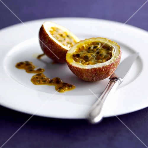 Passionfrucht, halbiert, auf Teller mit Messer