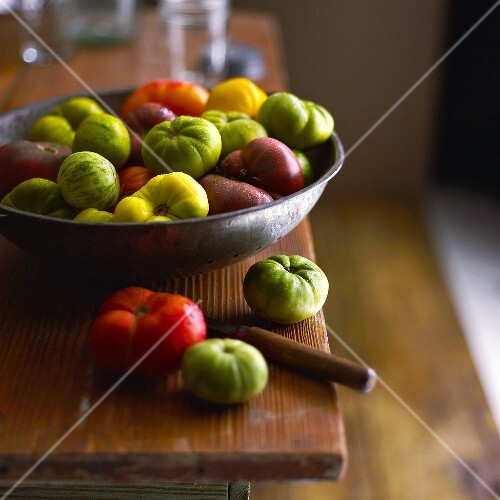 Bunte Heirloom Tomaten in und neben Schale auf Holztisch
