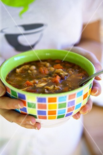Hände halten bunte Schale mit herzhafter Suppe