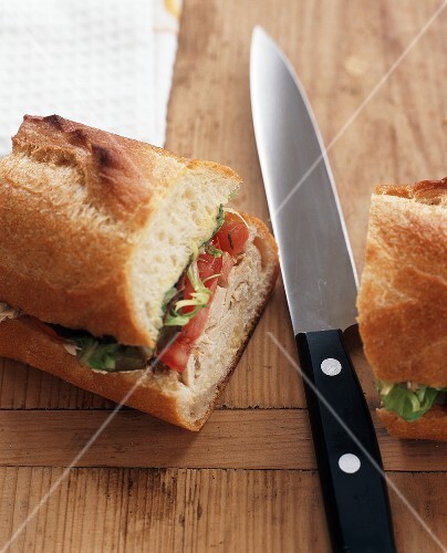 Turkey, Tomato and Lettuce Sandwich on a Baguette; Halved with Knife