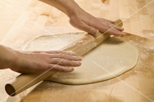 Hands Rolling Out Pizza Dough with a Wooden Rolling Pin