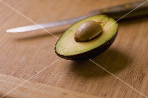 Half an Avocado with Pit on Cutting Board; Knife